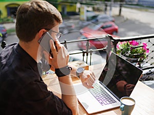 Portrait of successful young businessman speaking by phone while working in cafe outdoors