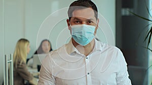 Portrait of successful young businessman wearing protective face mask looking into camera in corporate office