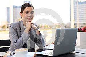 Portrait of successful young woman with laptop in street cafe