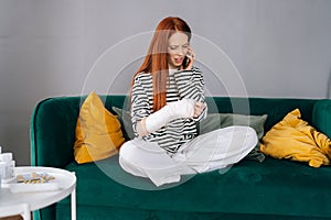 Portrait of suffering from pain injured young woman with broken arm wrapped in white gypsum bandage talking on