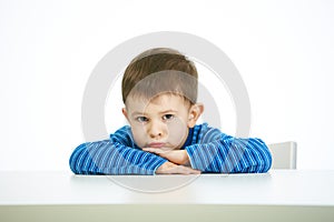 Portrait of sullen little boy sitting at table photo