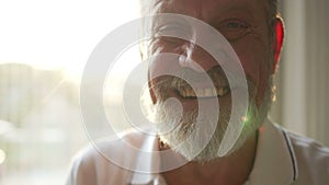 Portrait with sun glare of an elderly happy pensioner with glasses with a gray beard and a white T-shirt. Happy