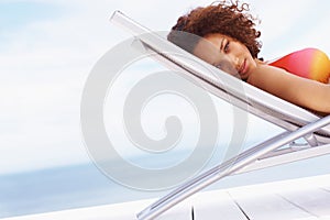 Portrait, sunbathing and black woman relax at beach for travel, summer or vacation on blue sky background. Face, tanning