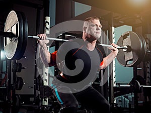 Portrait of super fit muscular young man working out in gym with barbell