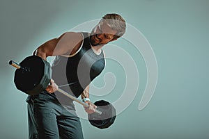 Portrait of super fit muscular young man working out in gym with barbell on gray background, copyspace.