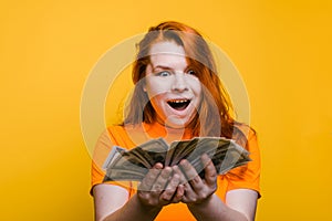 Portrait of a suprised young woman holding banknotes, yellow background.