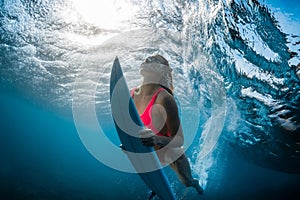 Portrait of surfer girl with surfboard dive underwater with under wave and sunlight in tropical ocean