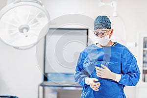 Portrait of surgeon in operating room. Cosmetic plastic surgeon wearing scrubs, goggles and gloves getting ready for surgery