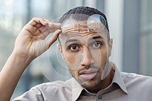 Portrait of surprised arab man looking amazed at camera and taking off round eyeglasses on blurred background. Shocked