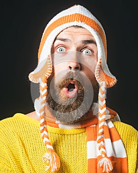 Portrait of surprised bearded man in yellow sweater, striped funny hat and scarf. Winter accessories. Handsome