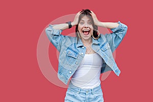 Portrait of surprised beautiful brunette young woman with makeup in denim casual style standing, holding her head, looking at