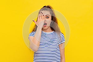 Portrait of surprised brunette girl, cover half of face and open mouth, looking at camera with one eye, checking vision, standing