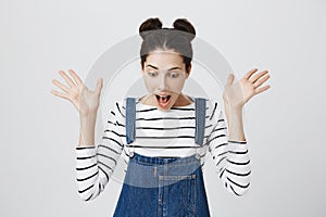 Portrait of surprised brunette girl in striped top and denim overall screaming in excitement, looking down. Cute female