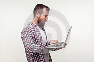 Portrait of surprised computer user, bearded man standing with laptop and typing on keyboard. studio shot isolated on white
