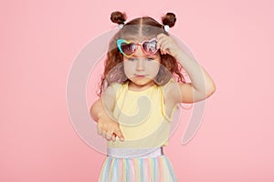 Portrait of surprised cute little toddler girl  in sunglasses over pink background.  Child model