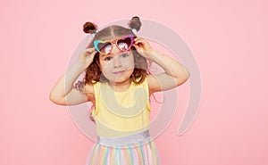 Portrait of surprised cute little toddler girl  in sunglasses over pink background.  Child model