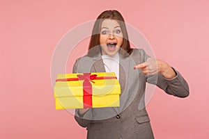 Portrait of surprised elegant businesswoman in suit jacket pointing at unexpected present and shouting in amazement photo