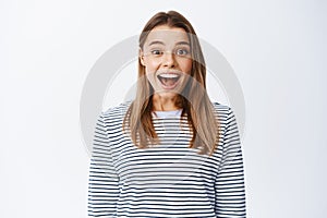 Portrait of surprised and excited blond girl open mouth fascinated, smiling amazed and looking at something cool
