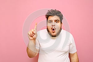Portrait of surprised fat man in white t-shirt and with beard on pink background, looks into camera with shocked face, and shows