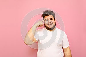 Portrait of surprised fat man in white t-shirt stands on pink background, looks into camera with shocked face and points finger at