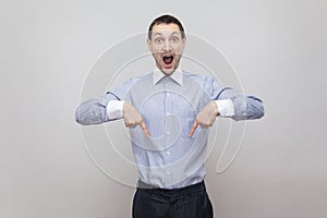 Portrait of surprised handsome bristle businessman in classic blue shirt standing and pointing at down copyspace and looking at