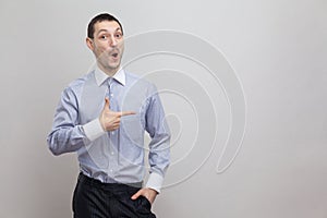 Portrait of surprised handsome bristle businessman in classic blue shirt standing and pointing at side copyspace and looking at