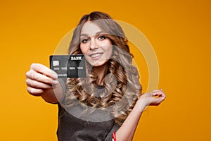 Portrait of a surprised happy girl holding shopping bags and showing credit card while looking at camera isolated over