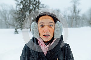 Portrait of surprised hispanic woman in winter clothes outdoors on a snowy day, looking shocked at the camera with open mouth on a