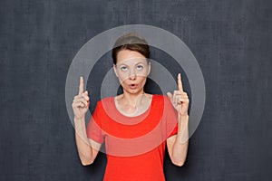 Portrait of surprised impressed girl pointing at copy space on top