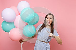Portrait of surprised joyful woman with opened mouth in blue dress pointing index finger on colorful air balloons