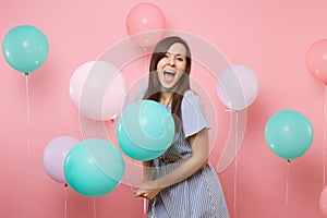 Portrait of surprised joyful woman with opened mouth wearing blue dress holding colorful air balloons on bright trending