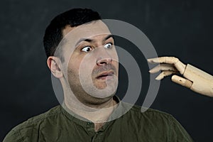 Portrait of a surprised man 30-35 years old, looking at a wooden model of an attacking hand. Concept: childhood fears in adults, a