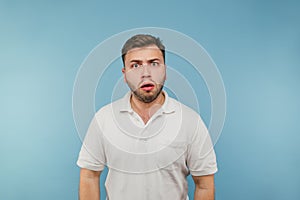 Portrait of a surprised man in a white T-shirt on a blue background looking at the camera with a shocked and scared face