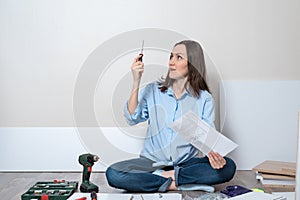 Portrait of a surprised, puzzled woman on the floor with a screwdriver and instructions for the Assembly of furniture