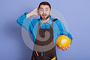Portrait of surprised shocked construction worker putting hand at back of his head, looking directly at camera with astonishment,