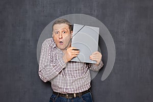 Portrait of surprised shocked man looking from behind folder