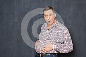 Portrait of surprised shocked man touching his big fat stomach