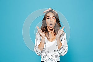 Portrait of surprised or shocked woman 20s wearing casual clothing raising up hands at face, isolated over blue background