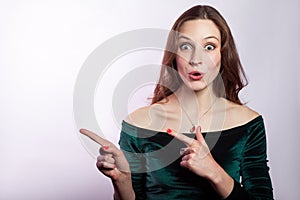Portrait of surprised shocked woman with freckles and classic green dress showing empty space with finger.