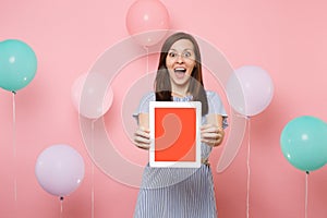 Portrait of surprised shocked young happy woman in blue dress holding tablet pc computer with blank empty screen on