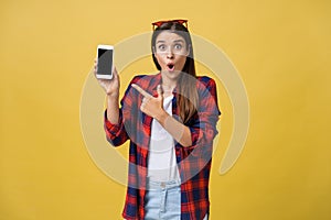 Portrait of a surprised woman in casual cloth showing blank screen mobile phone isolated over yellow background