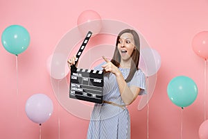 Portrait of surprised woman pointing index finger aside holding classic black film making clapperboard on pink
