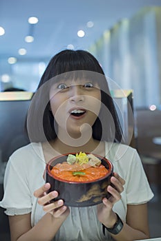 Portrait of surprised young asian woman holding japanese food dish