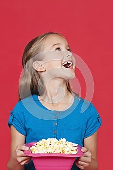 Portrait of surprised young girl holding popcorn container against red background