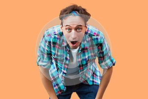 Portrait of surprised young man in casual blue checkered shirt headband standing with big eyes and open mouth and looking at