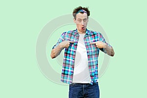 Portrait of surprised young man in casual blue checkered shirt and headband standing, pointing at himself and looking at camera
