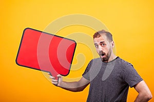 Portrait of surprised young man looking at the camera and holding a news board over yellow background