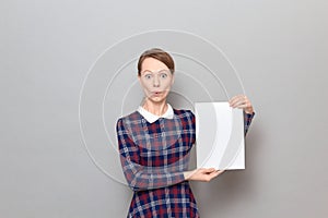 Portrait of surprised young woman holding white blank paper sheet