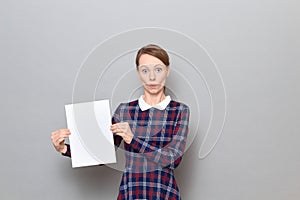 Portrait of surprised young woman holding white blank paper sheet