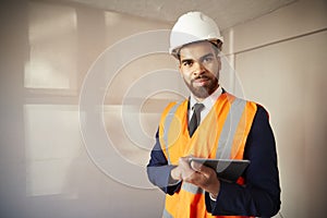 Portrait Of Surveyor In Hard Hat And High Visibility Jacket With Digital Tablet Carrying Out House Inspection